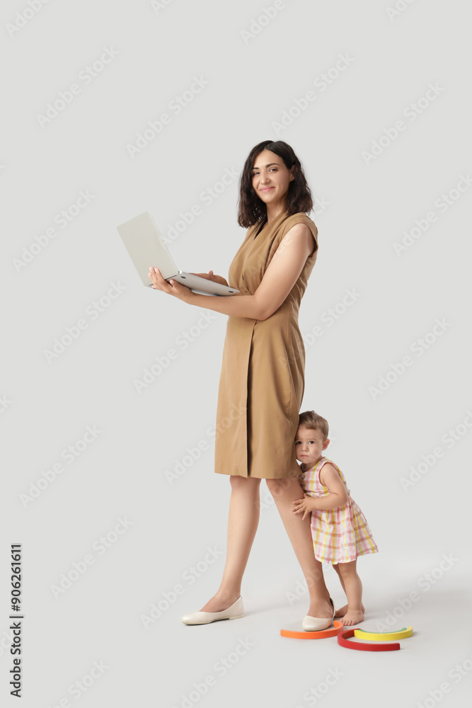 Fototapeta premium Working mother with laptop and her little baby on light background