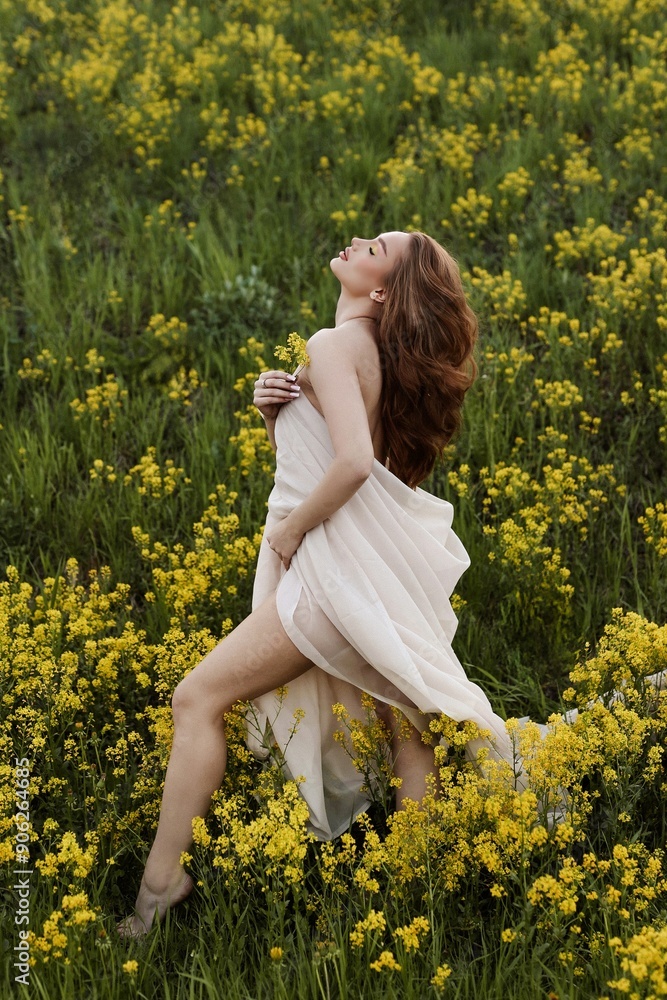 Fototapeta premium Young redhead model posing in field with yellow colors. Girls in white sheet