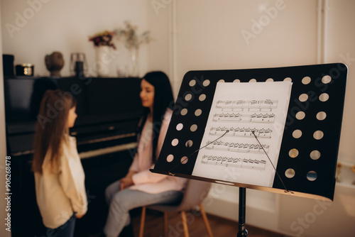 Indoor shot of pleasant looking woman speech pathologist having lesson with little girl, people sitting on comfortable sofa near window and training pronunciation of sounds and articulation.