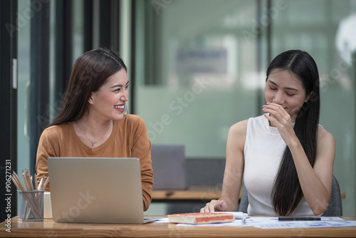 Two young Asian businesswomen discussed investment project work and planning strategy. Business people talk together on laptop computers at the office.
