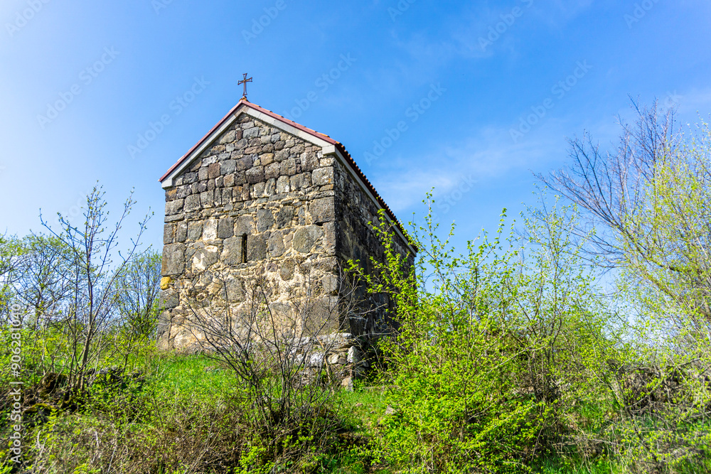 Side view of a small medieval church. Tiled roof, stone walls. Green grass meadow, bushes and trees. Samshvilde Side view of a small medieval church. Tiled roof, stone walls. Green grass meadow, bushes and trees. Samshvilde
