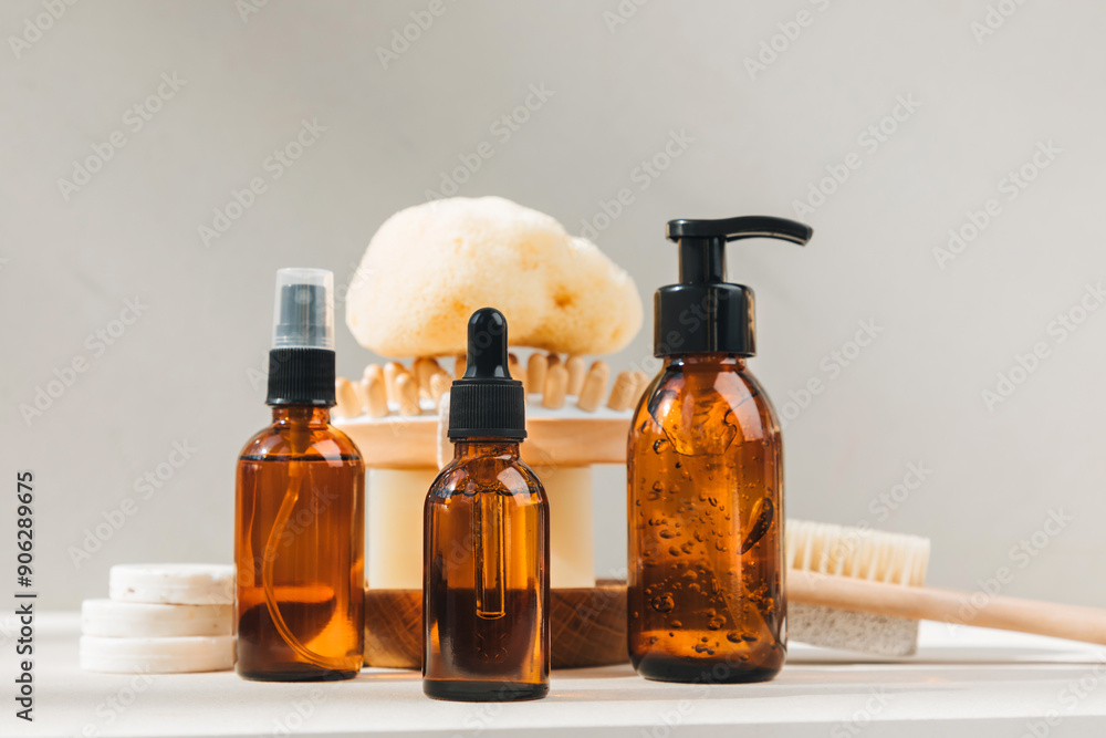 Set of natural cosmetics. Amber bottles with facial, bath liquid on a concrete background with natural bath sponge. Front view Set of natural cosmetics. Amber bottles with facial, bath liquid on a concrete background with natural bath sponge. Front view