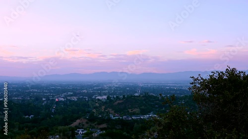 Overlooking the stunning cityscape from Mulholland Drive in Los Angeles, California, the sunset casts a warm glow over the urban skyline and surrounding mountains.