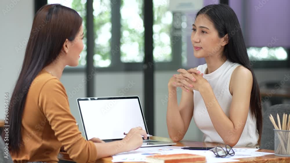 Two asian businesswomen communicating and sharing ideas while working together in the modern office. Two asian businesswomen communicating and sharing ideas while working together in the modern office.