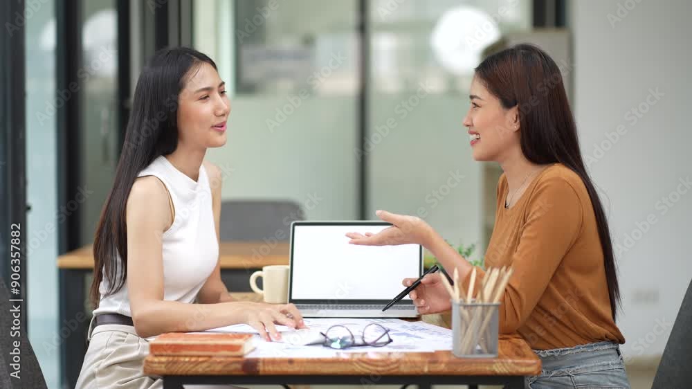 Two businesswomen reviewing and discussing data charts during meeting in modern office. Two businesswomen reviewing and discussing data charts during meeting in modern office.