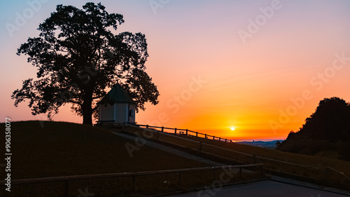 Alpine sunrise view with silhouettes of a tree and a chapel at Luitpoldchapel, Samerberg, Chiemgau, Rosenheim, Bavaria, Germany photo