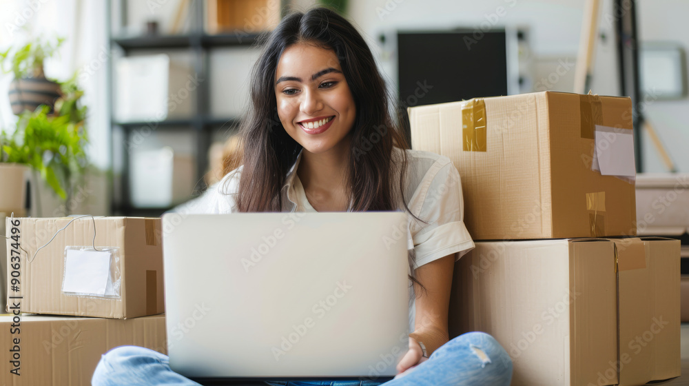 Smiling woman works on laptop surrounded by packed moving boxes, embodying excitement and fresh beginnings. Smiling woman works on laptop surrounded by packed moving boxes, embodying excitement and fresh beginnings.