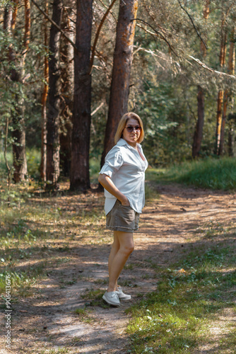 A cute girl in a white shirt and shorts walks along a forest path on a sunny day