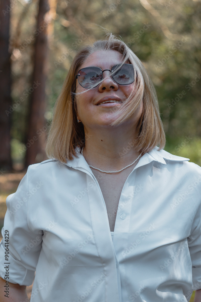 A cute girl in a white shirt and sunglasses walks through the forest, and the wind blows her short hair A cute girl in a white shirt and sunglasses walks through the forest, and the wind blows her short hair