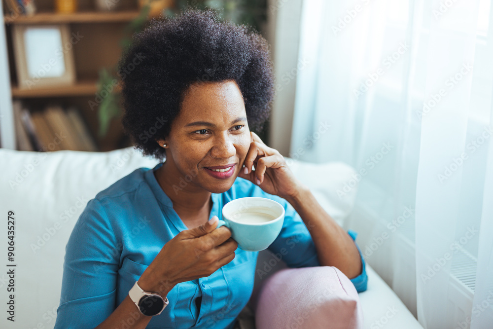 Portrait of an african woman sit on the sofa with coffee. Happy African american woman enjoying quiet time at home laughing, drinking morning coffee sitting on sofa. Portrait of an african woman sit on the sofa with coffee. Happy African american woman enjoying quiet time at home laughing, drinking morning coffee sitting on sofa.