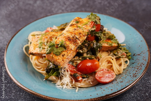 Salmon Fillet in creamy sauce with spaghetti, cream cheese and spinach and cherry tomatoes close-up on plate