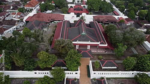 Aerial view of Yogyakarta Sultanate Palace. A traditional architectural complex with red roofs surrounded by lush greenery. The layout features pathways and manicured gardens.