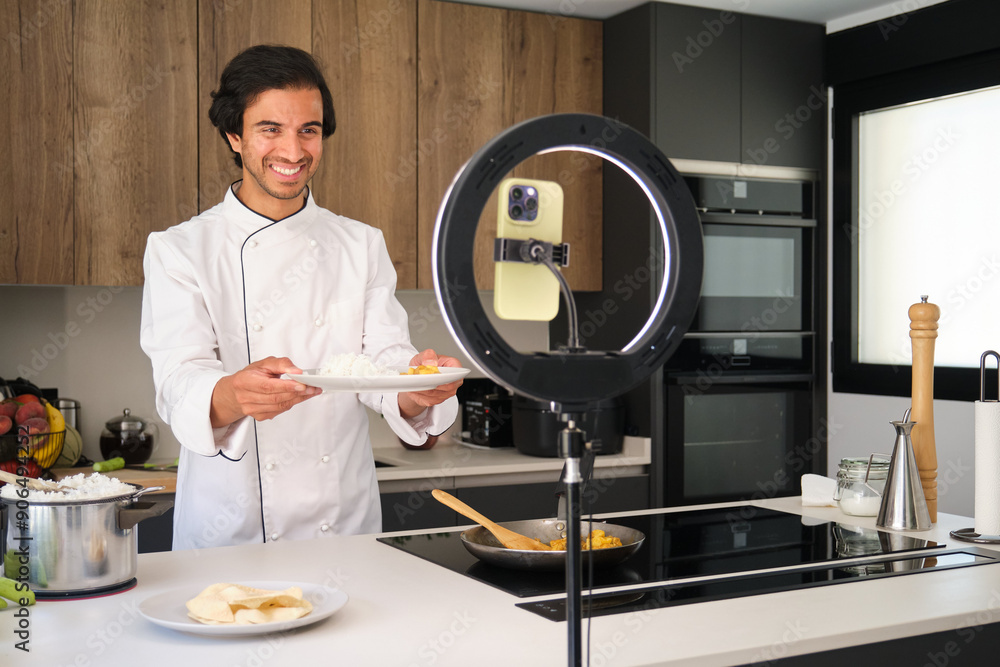 Indian chef is holding a plate and smiling while recording a culinary show in a modern kitchen