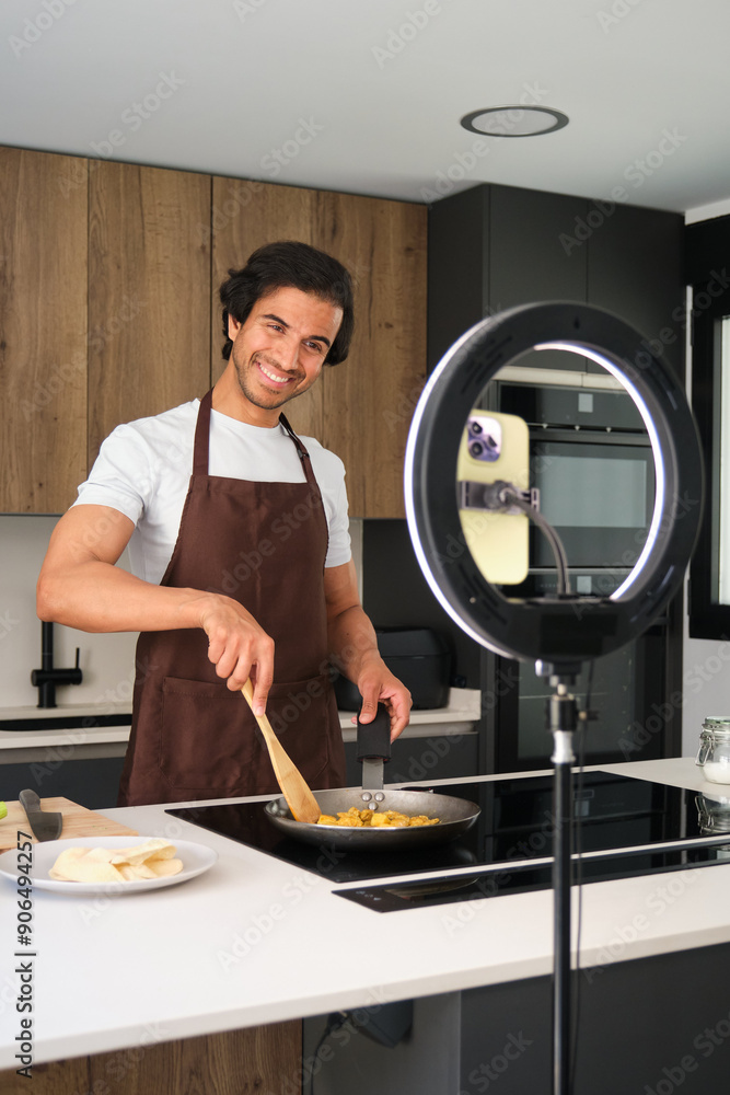 Young adult man is cooking indian food while recording a video blog about his recipe