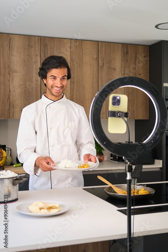 Indian chef is showing a plate with rice and curry in his kitchen, recording a video blog
