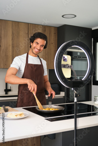 Obraz na płótnie Young adult man is cooking indian food while recording a video blog about his recipe w salonie