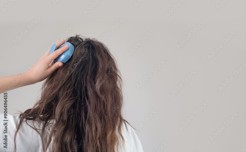 Naklejka premium Brunette with long, curly hair holds a head massager, performing a daily routine to boost hair growth.