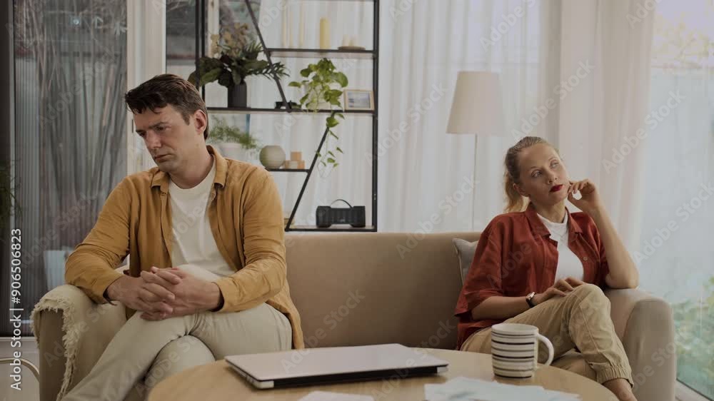 Medium long shot of middle-aged Caucasian spouses keeping silence when sitting on sofa after quarrel Medium long shot of middle-aged Caucasian spouses keeping silence when sitting on sofa after quarrel