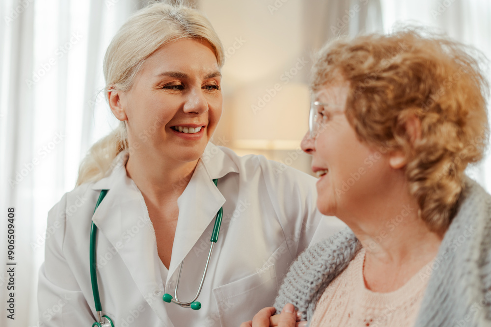 Fototapeta premium Female doctor smiling and comforting elderly female patient at home