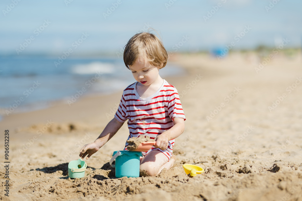 Cute little boy having fun on a sandy beach on warm and sunny summer day. Kid playing by the ocean. Summer activities for children Cute little boy having fun on a sandy beach on warm and sunny summer day. Kid playing by the ocean. Summer activities for children