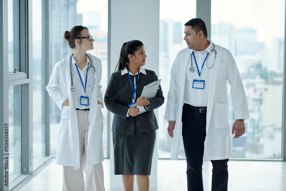 Doctors discussing working moments with manager while walking together along the corridor Doctors discussing working moments with manager while walking together along the corridor