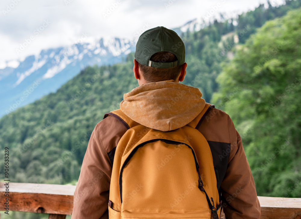 man with a yellow backpack in a cap enjoying a mountain view on a hike man with a yellow backpack in a cap enjoying a mountain view on a hike