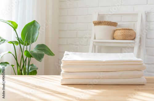 Photography Pile of folded bed sheets on wooden table in bright house room