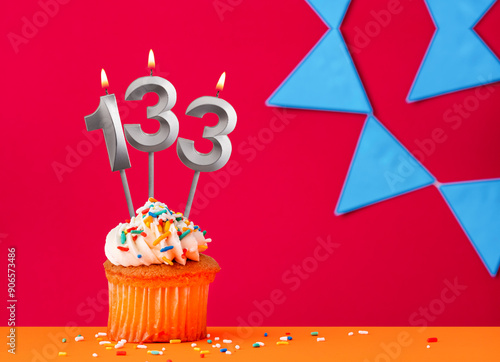 Birthday cupcake with candle number 133 on a red background with blue pennants