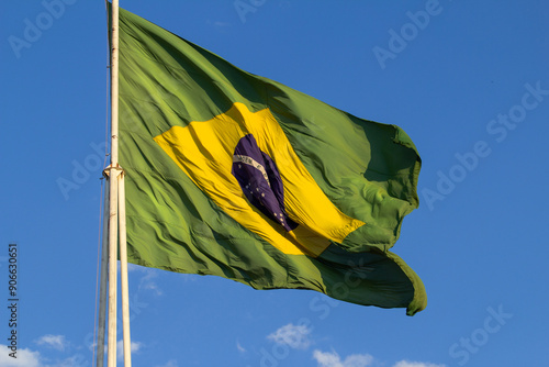 Close up em bandeira do Brasil hasteada balançando ao vento com céu azul ao fundo. photo