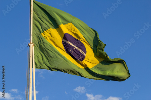 Close up em bandeira do Brasil hasteada balançando ao vento com céu azul ao fundo. photo