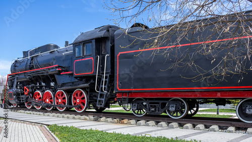 An old black steam locomotive.  
A large mainline passenger steam locomotive. Ancient railway transport. Transportation of goods by rail. A coal-fired steam locomotive. photo