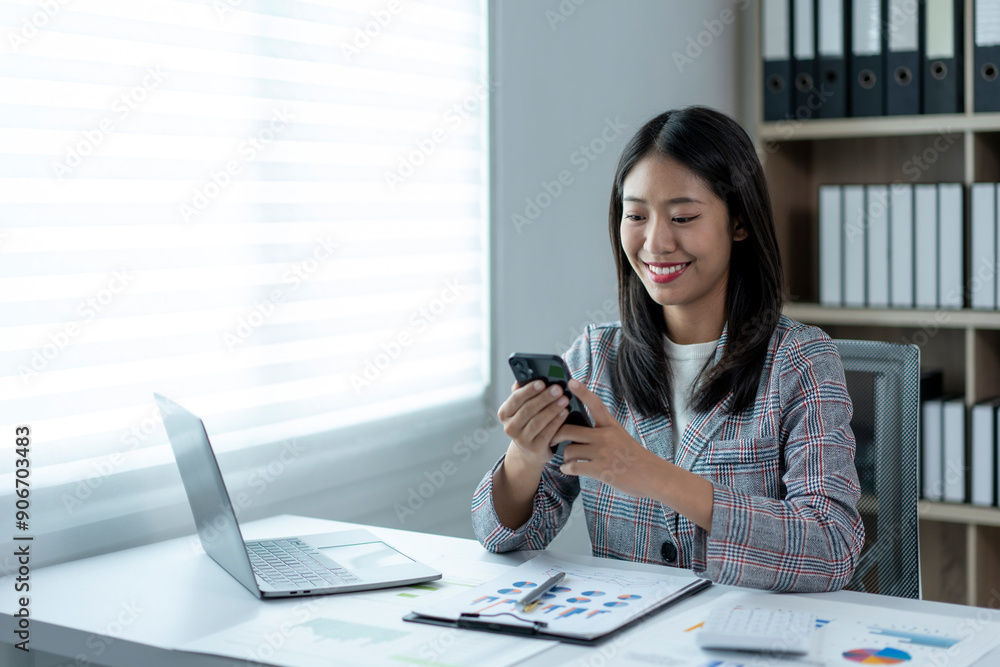 A woman is sitting at a desk with a laptop and a cell phone A woman is sitting at a desk with a laptop and a cell phone