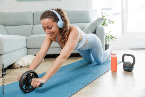 Young woman exercising at home with her pet. Listening to music with her headphones. Motivation to achieve results. Practicing sports is good for the body and mind. Healthy body, healthy mind photo