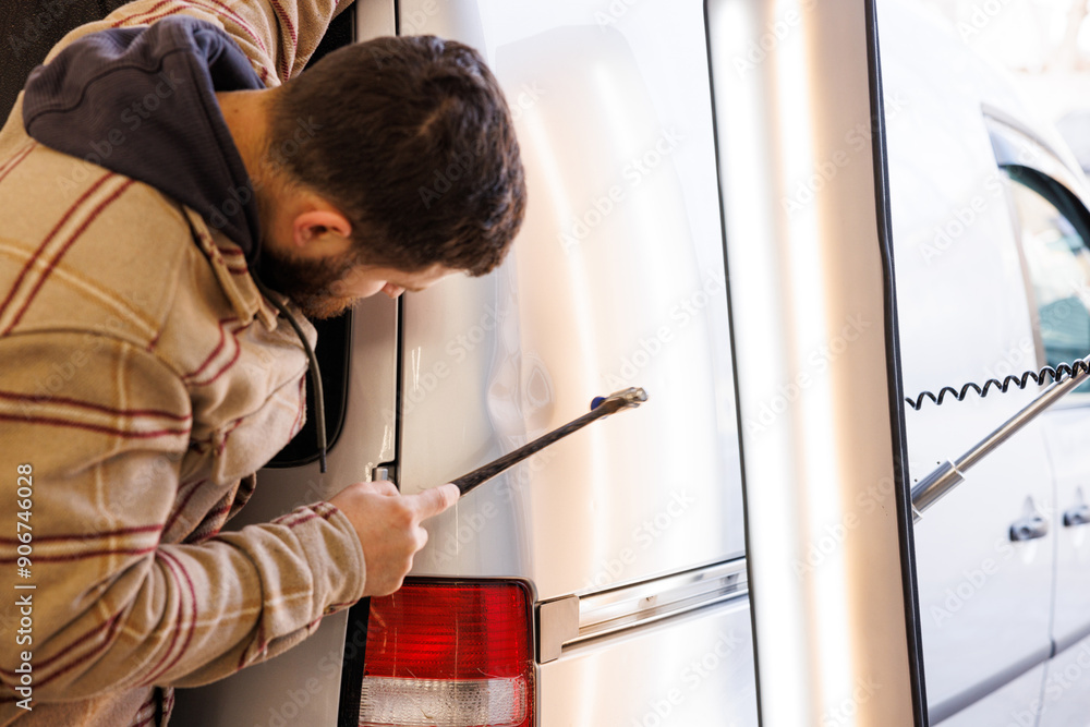 Caucasian boy uses the hammer to repair the wing of a car affected by a small accident