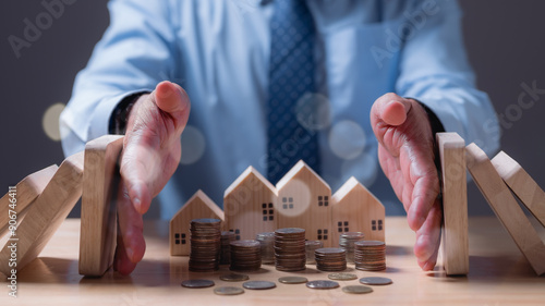 A man is holding up a stack of wooden blocks and coins, with the coins on top of the blocks. The man is wearing a blue shirt and a tie. Concept of financial stability and security