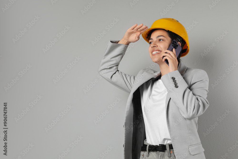 Engineer in hard hat talking on smartphone against grey background, space for text Engineer in hard hat talking on smartphone against grey background, space for text