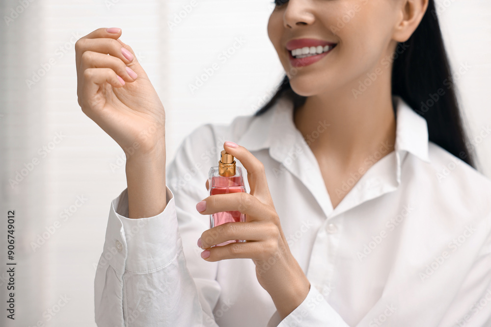 Fototapeta premium Smiling woman spraying perfume onto wrist at home, closeup