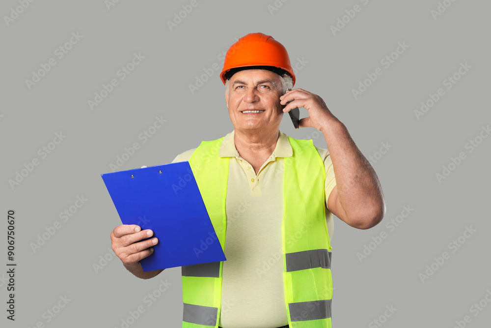 Engineer in hard hat with clipboard talking on smartphone against grey background Engineer in hard hat with clipboard talking on smartphone against grey background