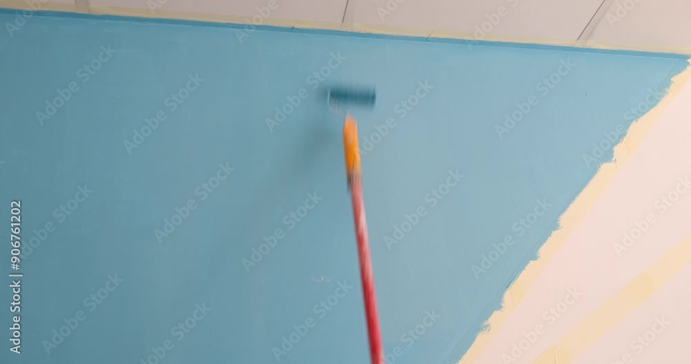 Painter paints wall blue with roller. Apartment renovation and wall painting concept Painter paints wall blue with roller. Apartment renovation and wall painting concept