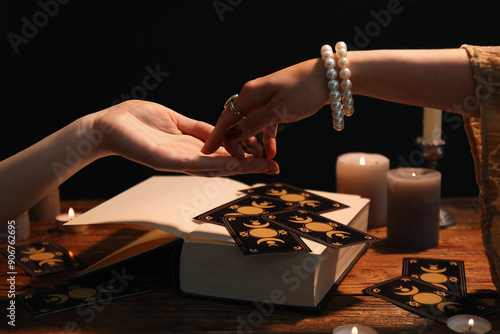 Fortune teller reading lines on woman's palm at wooden table, closeup. Chiromancy