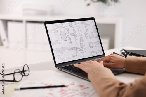 Cartographer working with cadastral map on laptop at white table in office, closeup