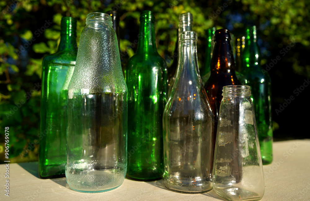 Glass bottle recycling. Empty glass bottles. Glass waste recycle. Glass bottles for reuse. Bottles waste reusable material. Bottles on a table in the garden against a background of green tree leaves Glass bottle recycling. Empty glass bottles. Glass waste recycle. Glass bottles for reuse. Bottles waste reusable material. Bottles on a table in the garden against a background of green tree leaves
