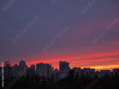 Amazing violet, purple, red and yellow sunset over Kyiv city with buildings, observation wheel and dome church on the horizon. Industrial cityscape of high-rise blocks against backdrop of scenic sky.