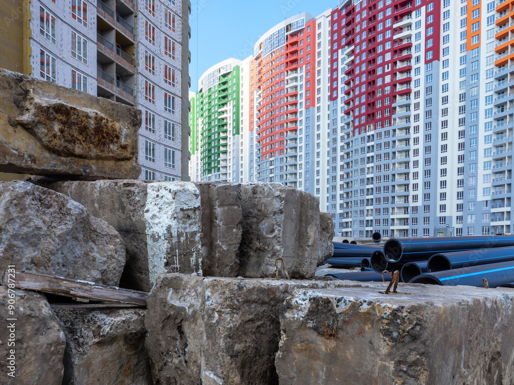 A building site with huge concrete blocks and big black pipes in the foreground and new colorful high-rise buildings in the background in Kyiv, Ukraine. New district under construction concept.