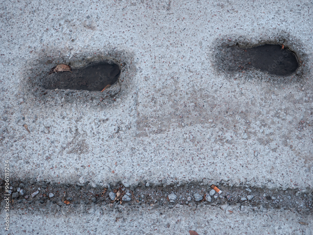 Deep footsteps and bike tire print embedded in wet cement and filled with water after the rain, and autumn leaf floating in it.