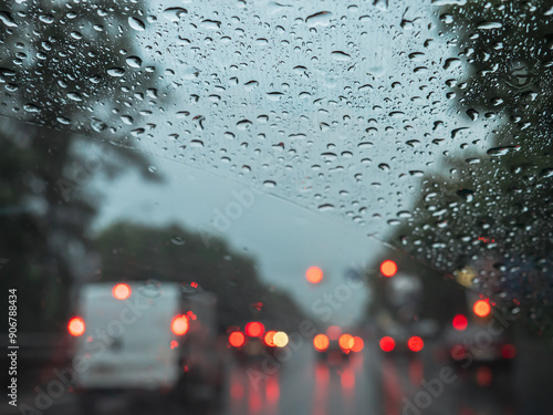 Obraz na płótnie Closeup of rain drops on a windshield, and blurry road traffic with cars and red and orange lights. View from the driver's seat. w salonie
