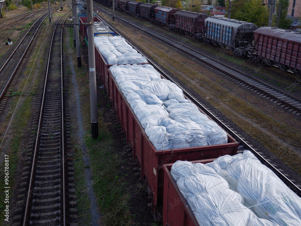 A long goods freight train with wagons without roofs loaded with huge white sacks and waiting at the station in Kyiv city, Ukraine.