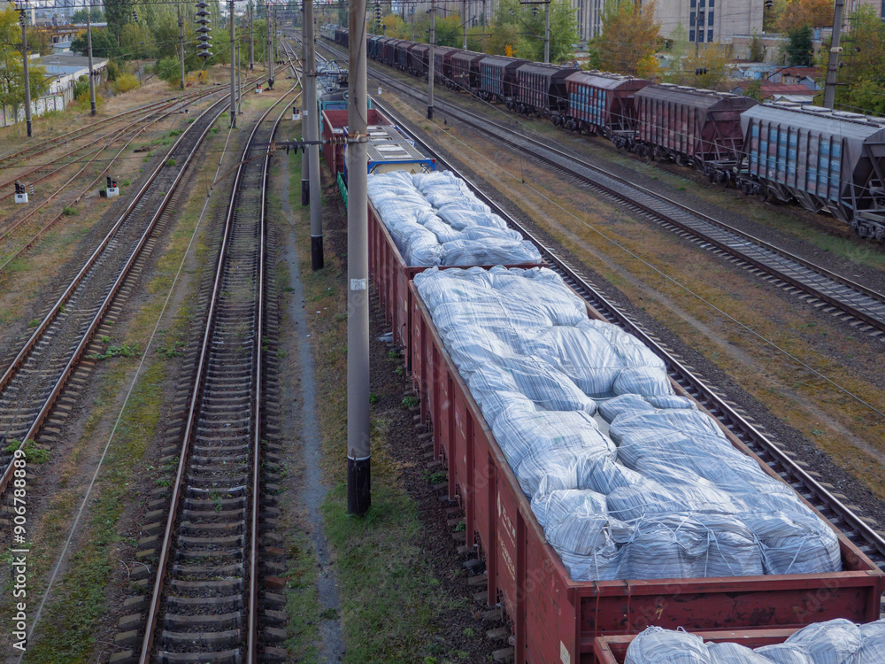 A long goods freight train with wagons without roofs loaded with huge white sacks and waiting at the station in Kyiv city, Ukraine.