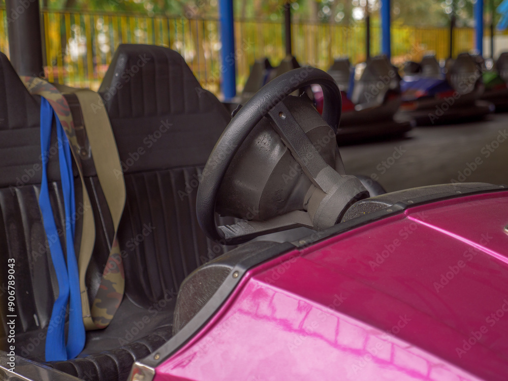 Closeup of a wheel and two seats of an electric old-fashioned bumper car and a row of autos standing behind in a city amusement park. Traditional family entertainment and active leisure time outdoors.
