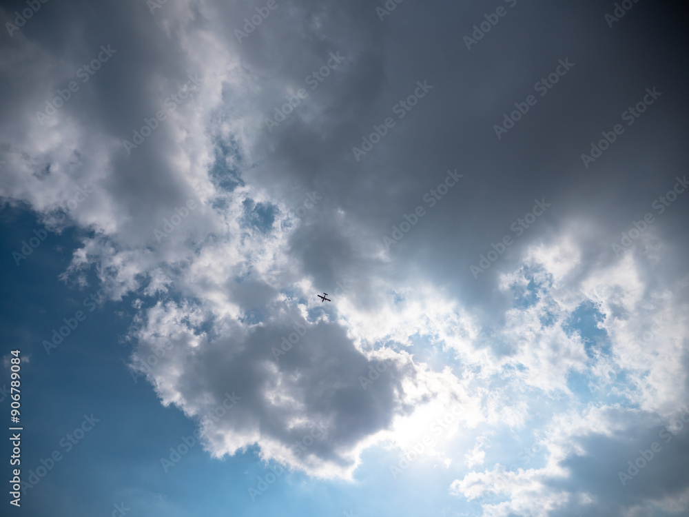 Airplane flying high up in the sky below dark blue stormy clouds with sun shining through them.